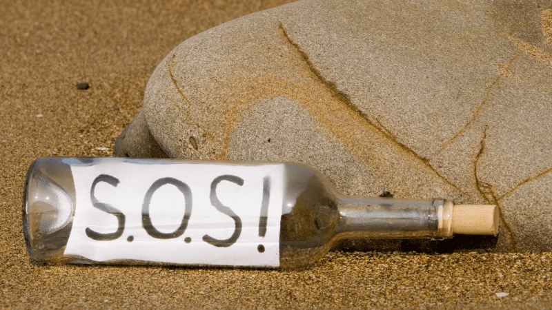 Glass bottle on the beach with S.O.S. written on a paper inside the bottle