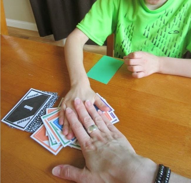 Student and adult slapping their hands on a pile of colorful cards (Verb Tenses)