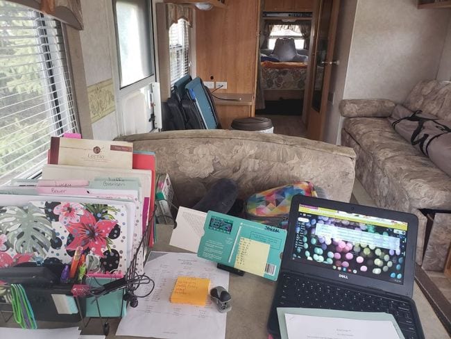 Interior of an RV with a desk set up for mobile teaching including a laptop, folders, and EZGrader