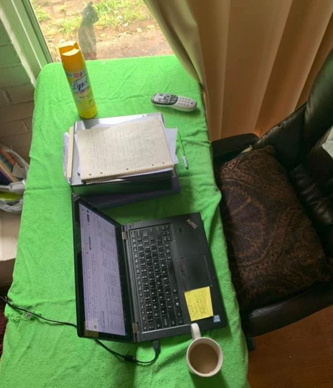 Laptop on table covered with green cloth, computer chair and can of Lysol spray