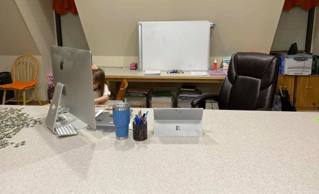 Apple computer on desk with computer chair and small child in background