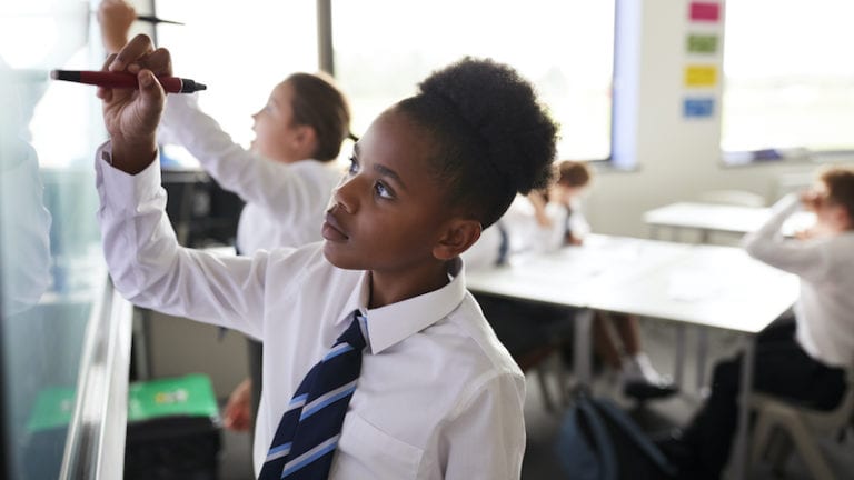 Female High School Students Wearing Uniform Using Interactive Whiteboard During Lesson.