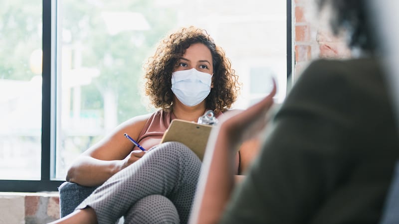 A female counselor attentively listening to a patient while wearing a protective mask.