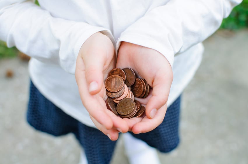 A handful of pennies rest in a girl's cupped hands.