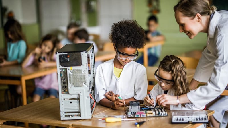A STEM teacher teaching two young kids about programming the inside of a desktop computer.