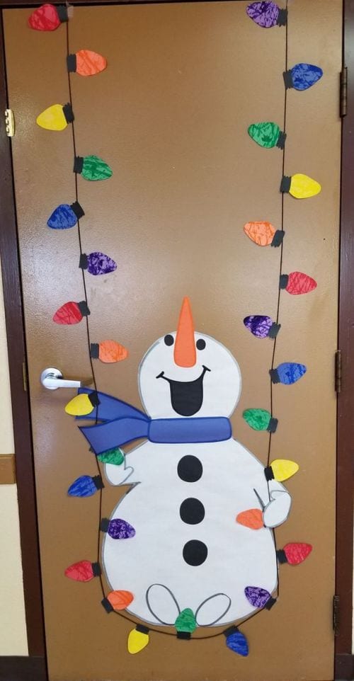 Classroom door decorated with a snowman sitting on a string of colored lights