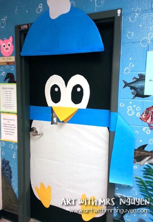 A classroom door is decorated to look like a large penguin wearing a blue hat and scarf.
