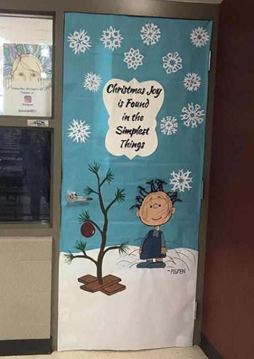 A classroom door is decorated with the characters from Charlie Brown and the famous shabby Christmas tree from the movie.