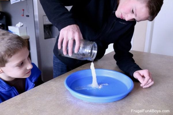 Young boy watching an older boy pour "hot ice" from a jar onto a plate