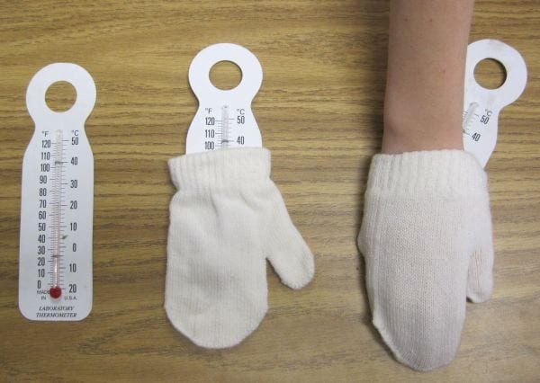 Thermometer and pair of white mittens, with a child's hand inside one mitten along with a thermometer