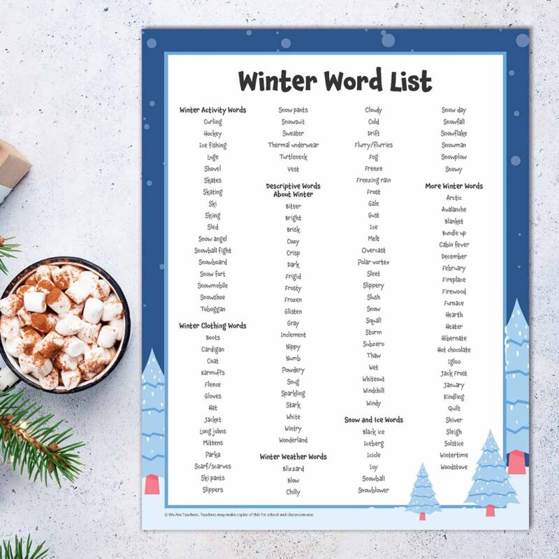 Winter words printable sheet next to a sprig of greenery and a mug of hot cocoa with marshmallows (square image).