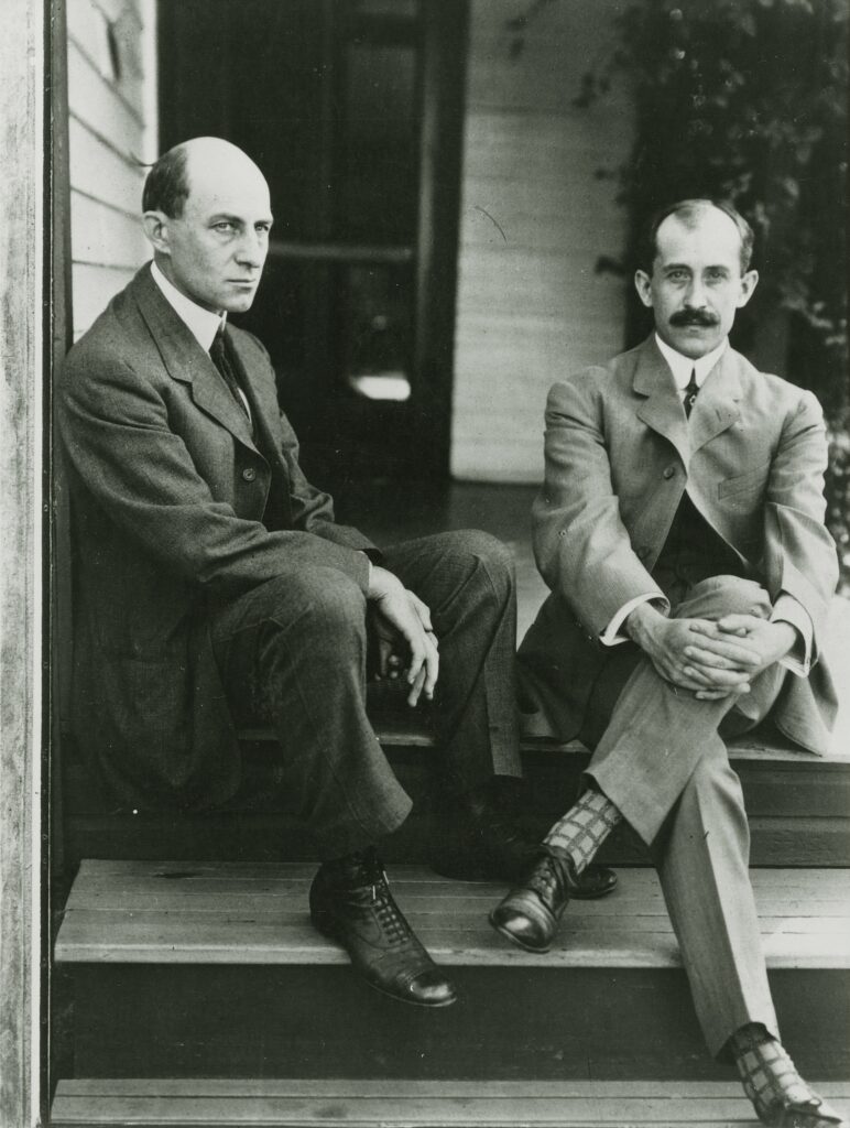 Two men are seen wearing suits and sitting on steps in a photograph from 1910. 