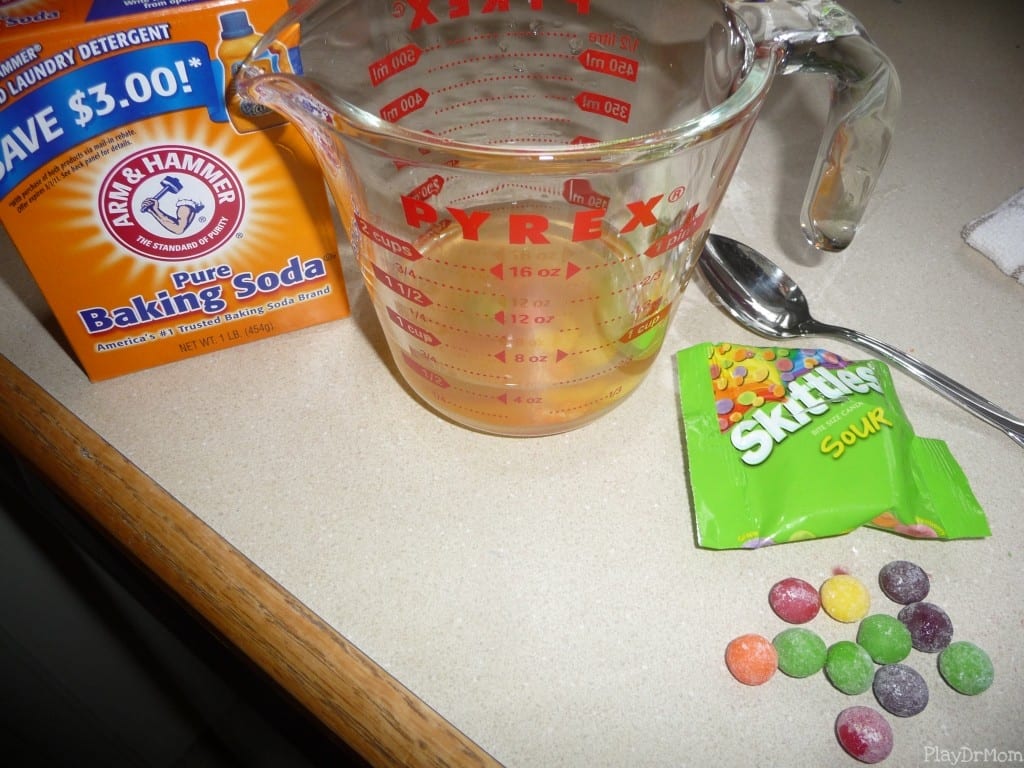 a box of baking soda, glass pyrex measuring cup, spoon and an open package of Sour Skittles on a countertop