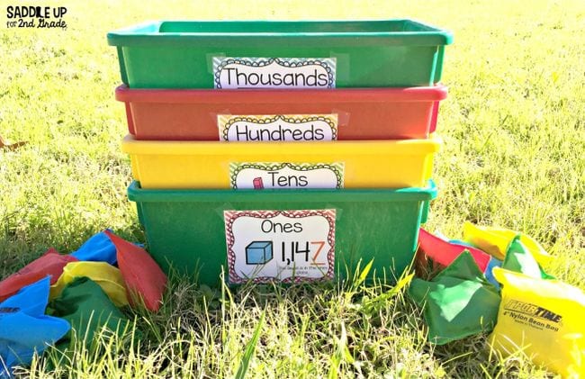 Plastic bins labeled thousands, hundreds, tens, and ones sitting on the grass with beanbags (Active Math Games)