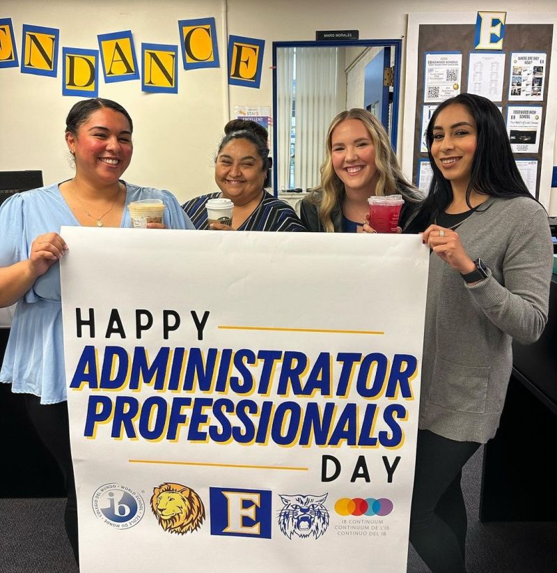 A group of school office workers standing with a sign saying "Happy Administrative Professionals Day"