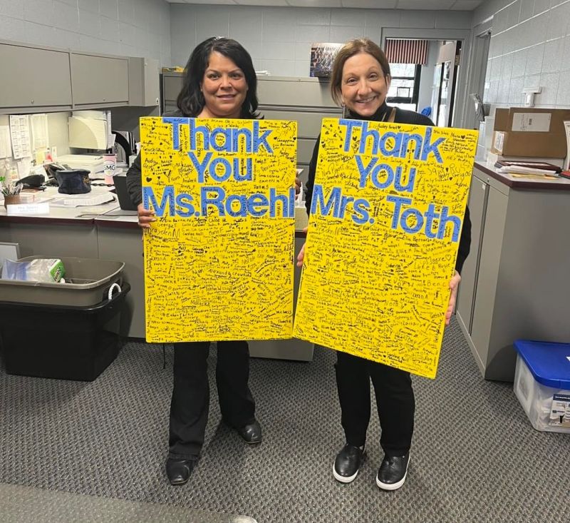Two school administrative professionals holding thank you signs with student signatures and notes