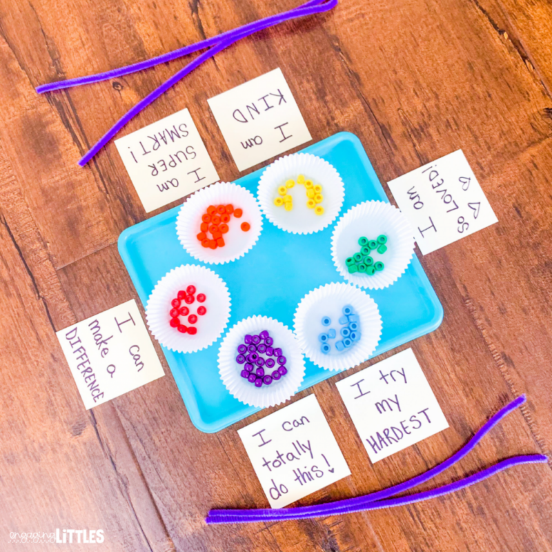 A tray holding cupcake papers filled with different color pony beads with affirmation cards and pipe cleaners around the edge