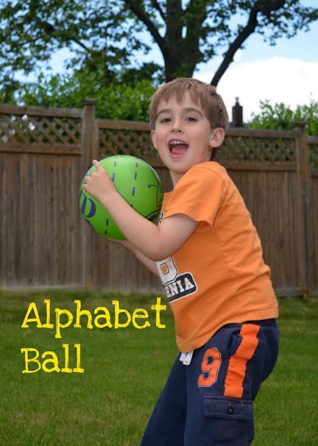 Boy in backyard playin alphabet ball, s an example of gross motor activities.