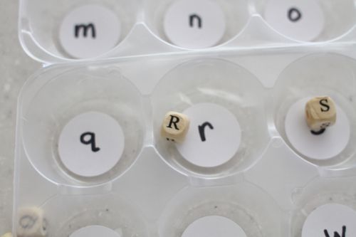A divided container with letters written in each compartment with corresponding beads in a few as an example of alphabet activities
