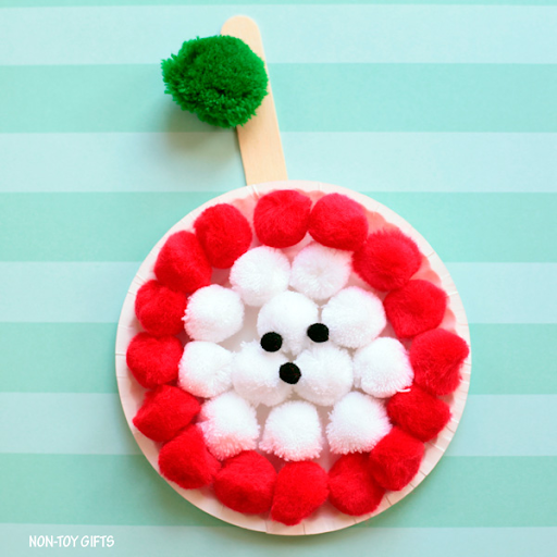Apple core pom pom plate craft with red pompoms in a circle and white pom poms in the middle of it, black paper for seeds, and a green pom pom stem.