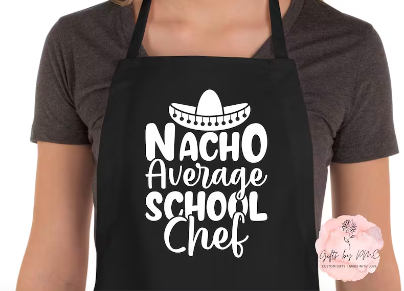 A woman wearing a black apron that says "Nacho average school chef"
