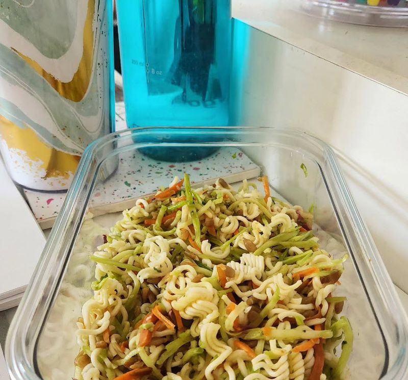 Green glass container with Asian salad and a blue water bottle