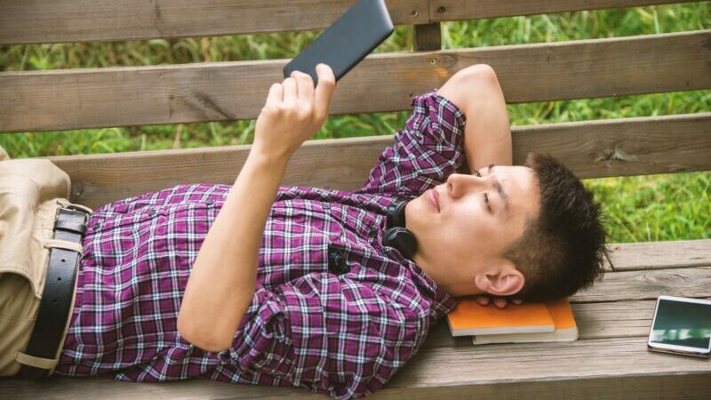 asian teen reads an ereader on a park bench teens are reading less