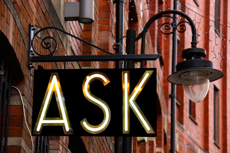 Lighted sign reading ASK hanging from a building