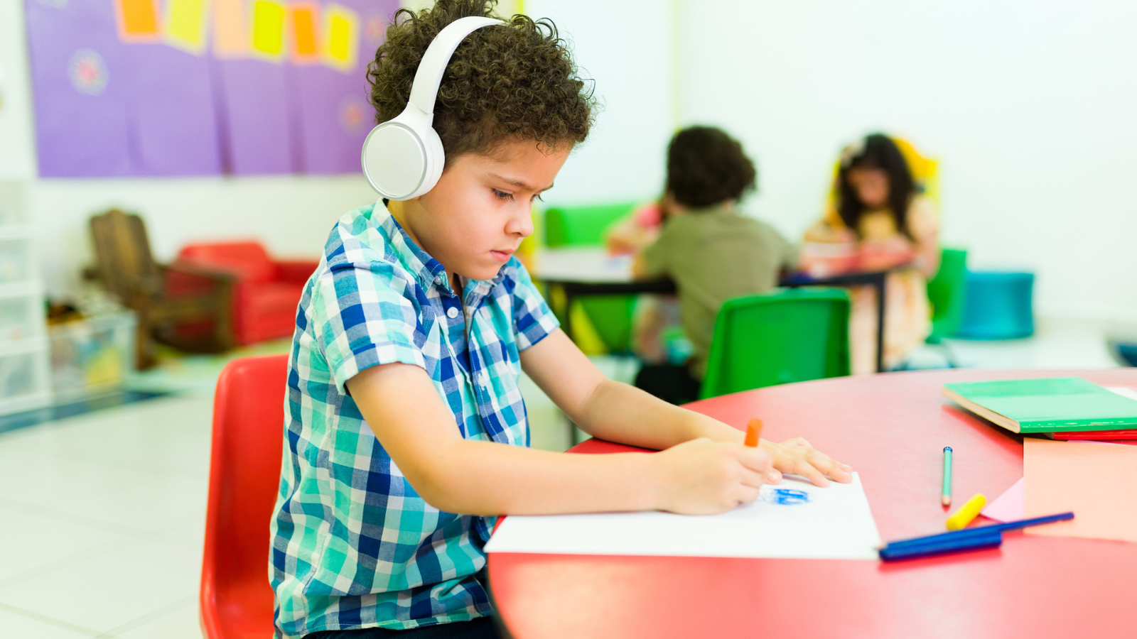 Autistic boy wearing headphones in classroom and coloring, as an example of autism resources for teachers
