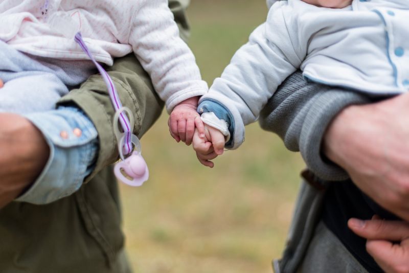 Two babies holding hands while being held by adults