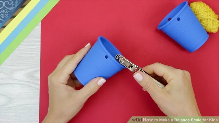 Hands are shown punching holes into small plastic cups (first grade science experiments)