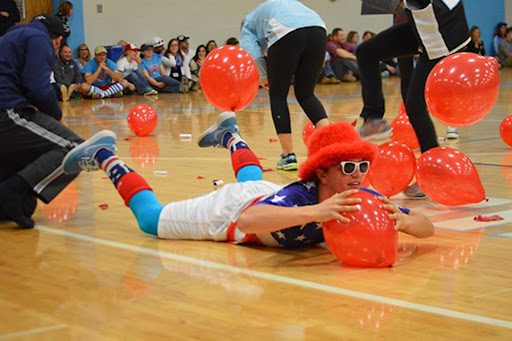 Pep rally activities can include balloons like this one which shows a boy on the floor of a gym trying to pop an orange balloon.