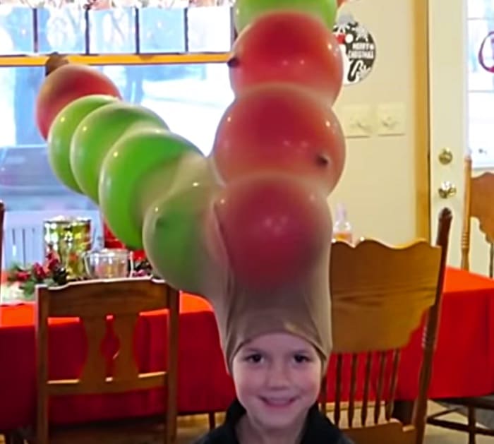 A little child is shown from the neck up. He is wearing a pair of nylons on his head that have been filled with balloons to look like antlers in this example of minute to win it games.