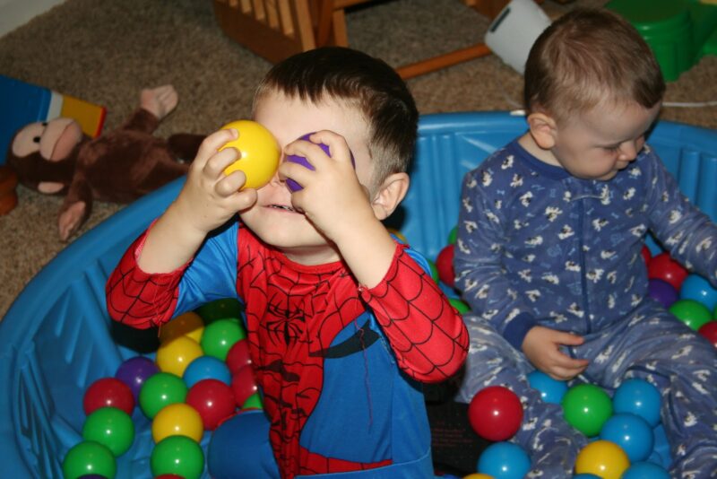 Two little kids play in a kiddie pool filled with brightly colored plastic balls.