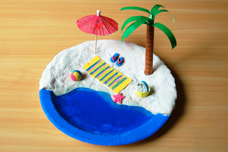 clay has been used to create sand on a paper plate. The ocean is painted blue. Various beach scene items have been added like a palm tree, umbrella, etc. (ocean activities)