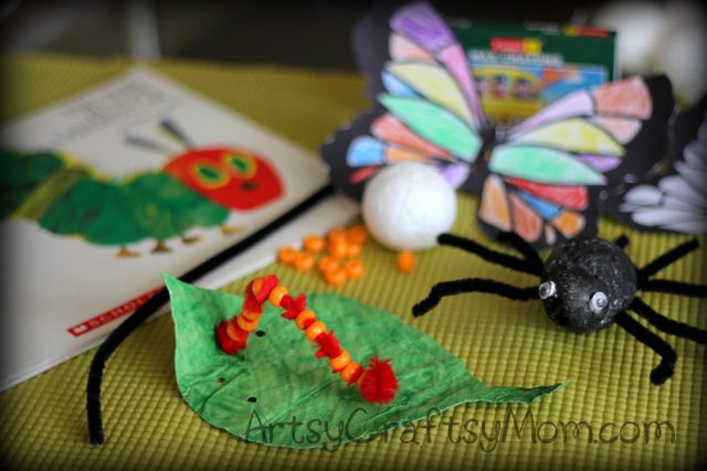 The Very Hungry Caterpillar book is in the background on a table. A green leaf has a caterpillar on it that is constructed from a red pipe cleaner and beads. (very hungry caterpillar activities)