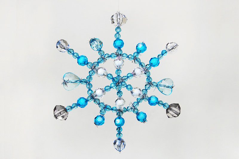 A snowflake is shown that has been created using pipe cleaners and different blue and clear beads. 
