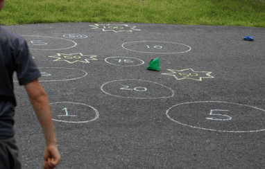 Kid throwing bean bags at targets drawn with chalk, as an example of gross motor activities.