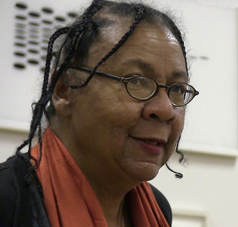 A woman is shown in a color photo from the neck up. She is wearing a coral scarf and thin wire frame black glasses.