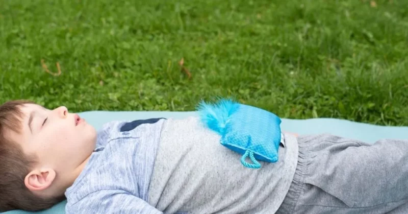 A young boy lays in a field with a pillow on his belly