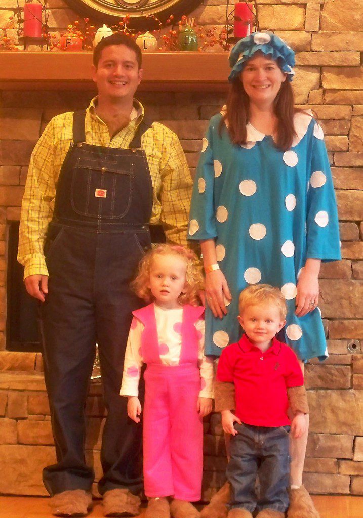 A family is dressed up, the father is wearing overalls and a yellow shirt, the mother is wearing a blue and white polka dot dress, the daughter is in pink overalls, and the little boy is in jeans and a red shirt.