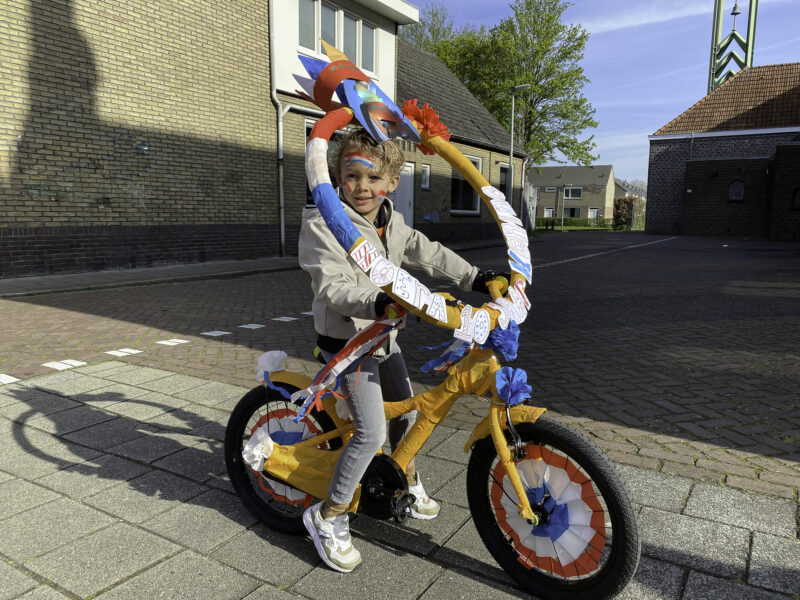 Little boy is showing his decorated bicycle at Kingsday