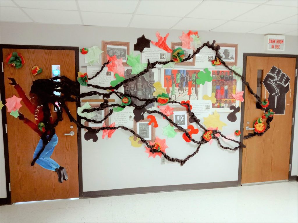 A hallway is connected by two doorways. The door on the left has a side profile of a girl whose dreadlocks are running across the hallway into the second door. There is information on artists in the hallway.