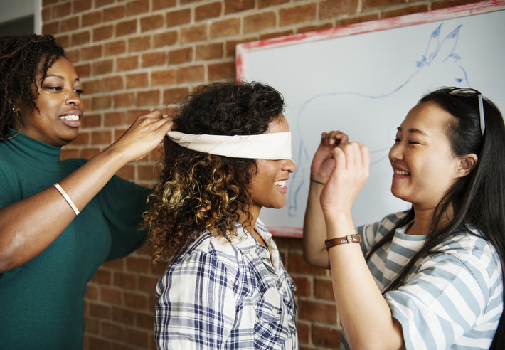 teacher tying a blindfold onto students while another student helps adjust the bandana