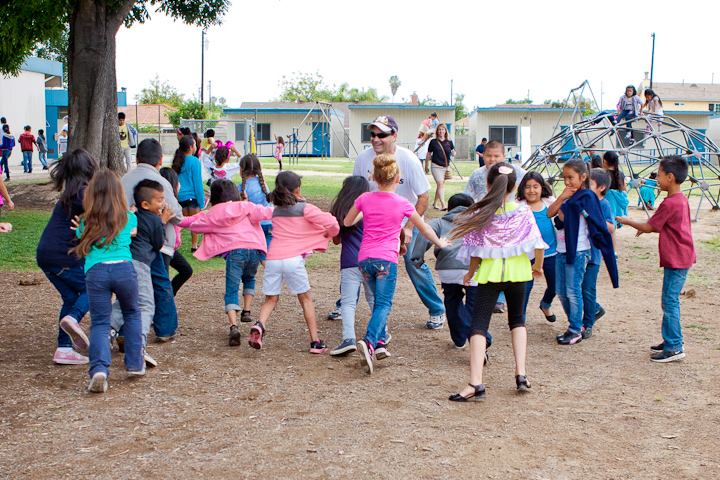 A large group of elementary school aged children are holding hands and running outside (elementary PE games)