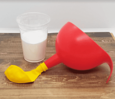 A plastic cup of baking soda next to a balloon attached to a funnel