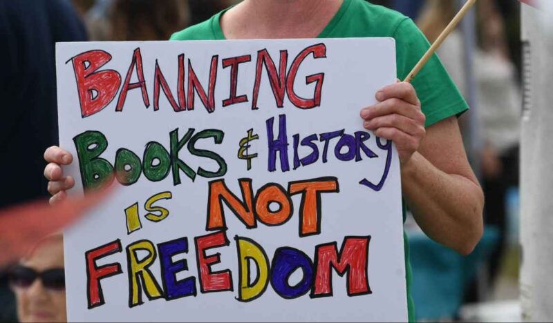woman holding sign that reads banning books and history is not freedom