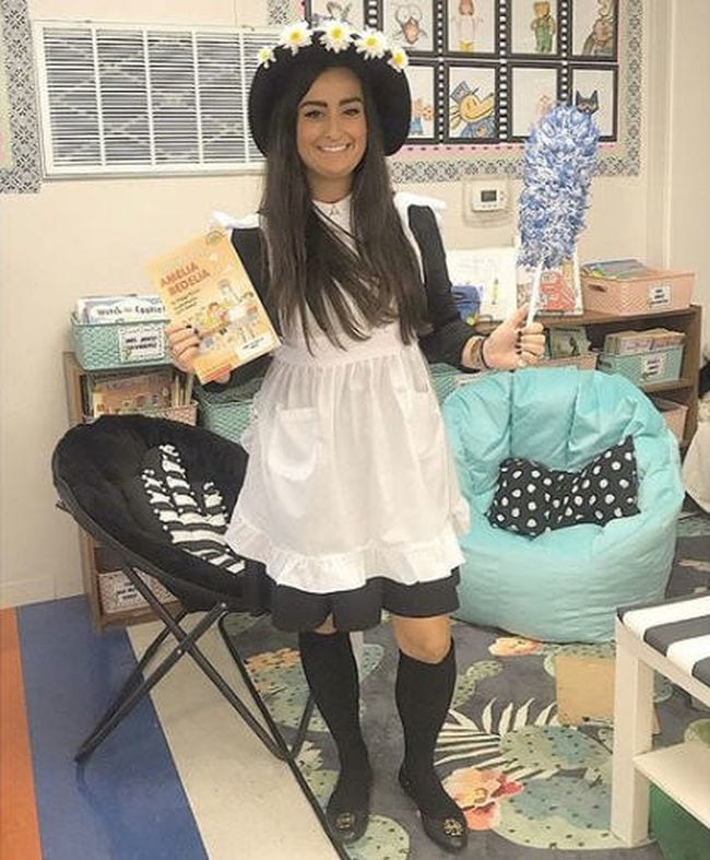 Book character costume ideas like this one shows a woman wearing black dress, white apron, black hat with daisies, and carrying a feather duster (Book Character Costume Ideas)