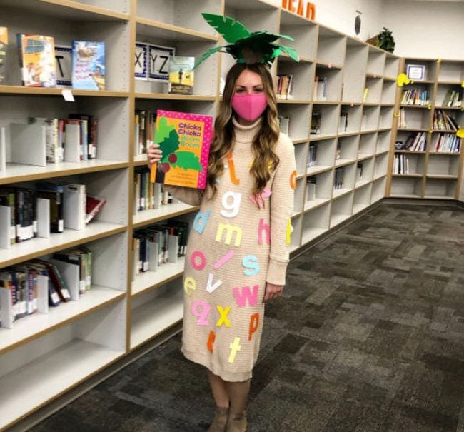 Woman wearing palm leaves on her head and covered in alphabet letters, carrying the book Chicka Chicka Boom Boom- book character costume