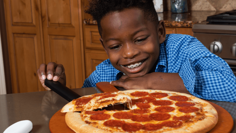 African American boy wearing braces smiling and looking at pepperoni pizza from Little Caesars Fundraising